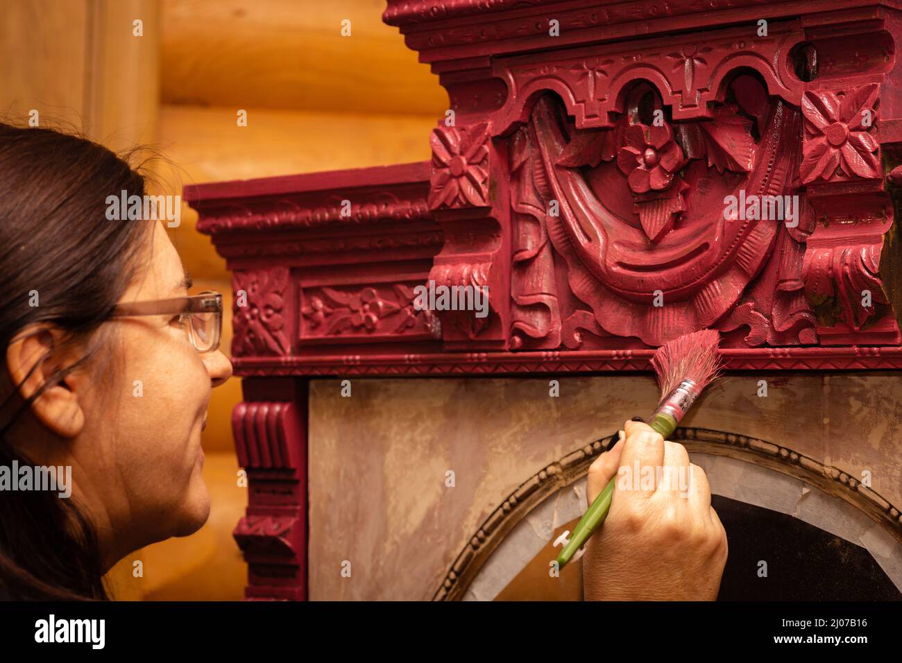 Finitura femminile ornamenti superiori in legno armadio in rosso con pennello in mano. Dare nuova vita alle cose antiche. Ristrutturazione di mobili per la casa Foto Stock