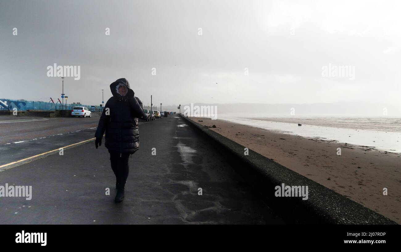 Donna che cammina con il vento a corda sul lungomare di Ayr Foto Stock