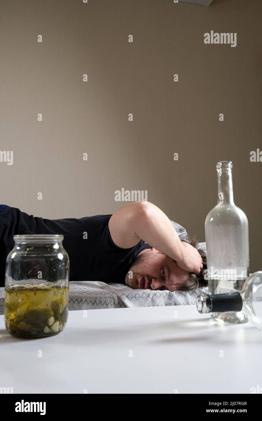 Un uomo ubriaco si trova a letto, tenendogli le mani in testa. Hangover, delirio alcolico. Foto Stock