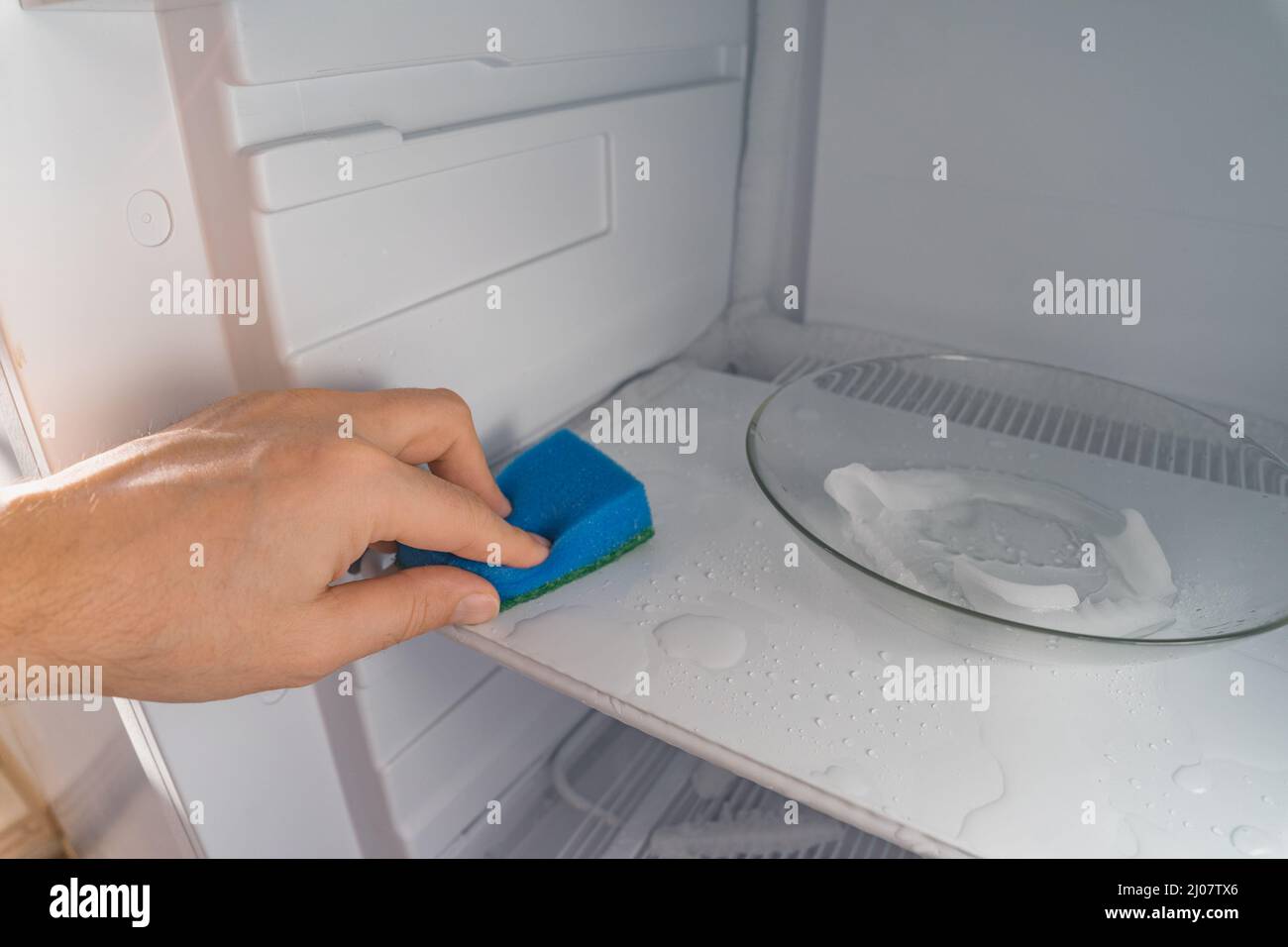 Sbrinamento e pulizia del congelatore. Un uomo pulisce l'acqua di fusione con una spugna. Profondità di campo poco profonda. Spazio per il testo. Foto Stock
