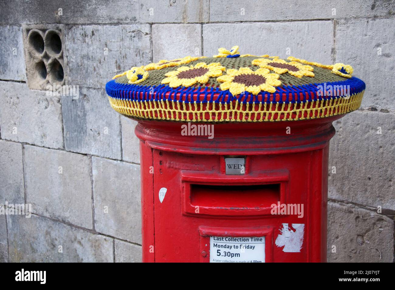 Colori ucraini blu e giallo: Cappello di lana lavorato a maglia decorare un pillarbox rosso. In solidarietà con il popolo ucraino. Dorchester, Dorset, Regno Unito. Foto Stock