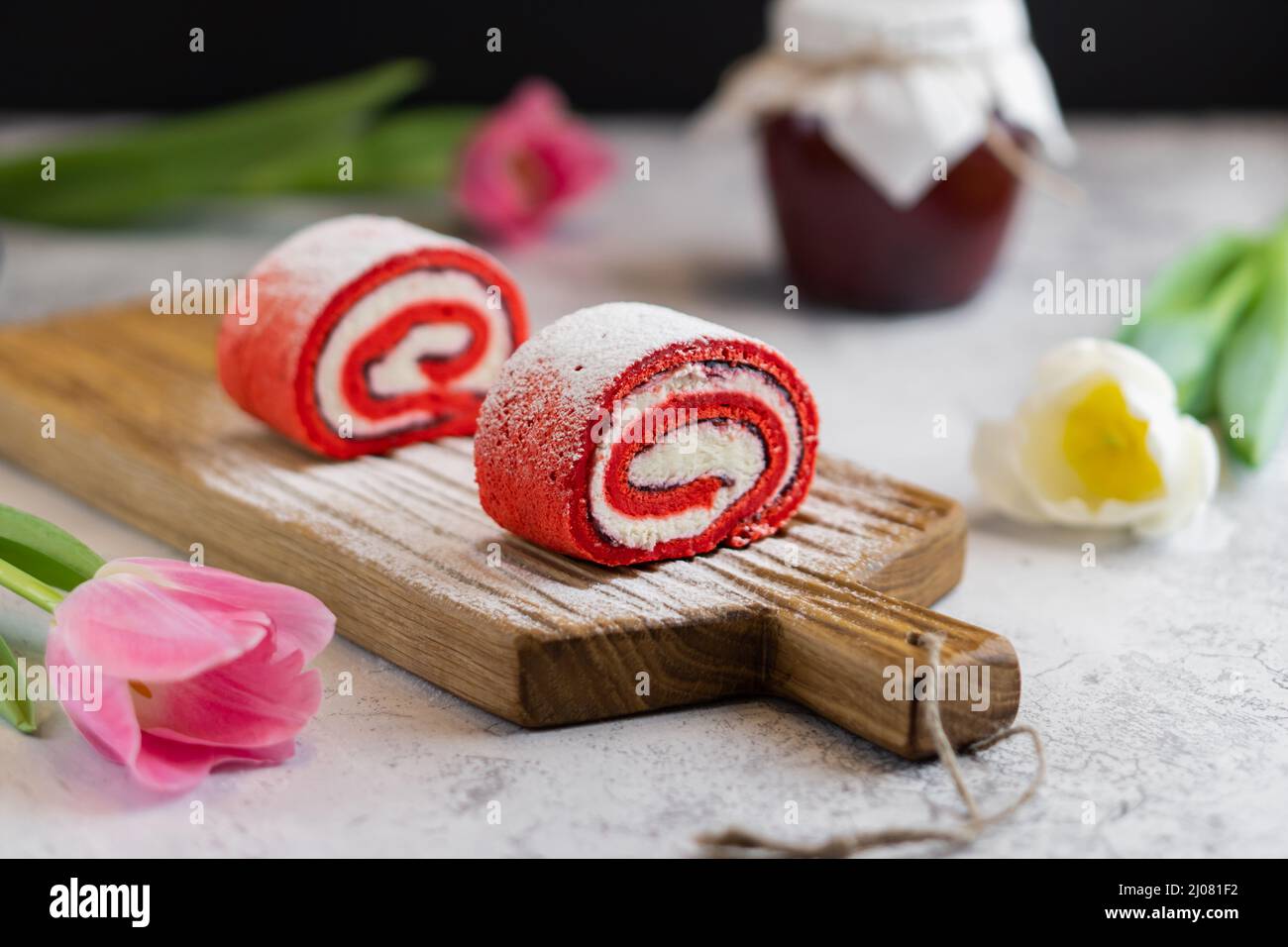 Cupcake rosa fatti in casa su tavola di legno con tulipani primavera e vasetto di marmellata su sfondo grigio Foto Stock