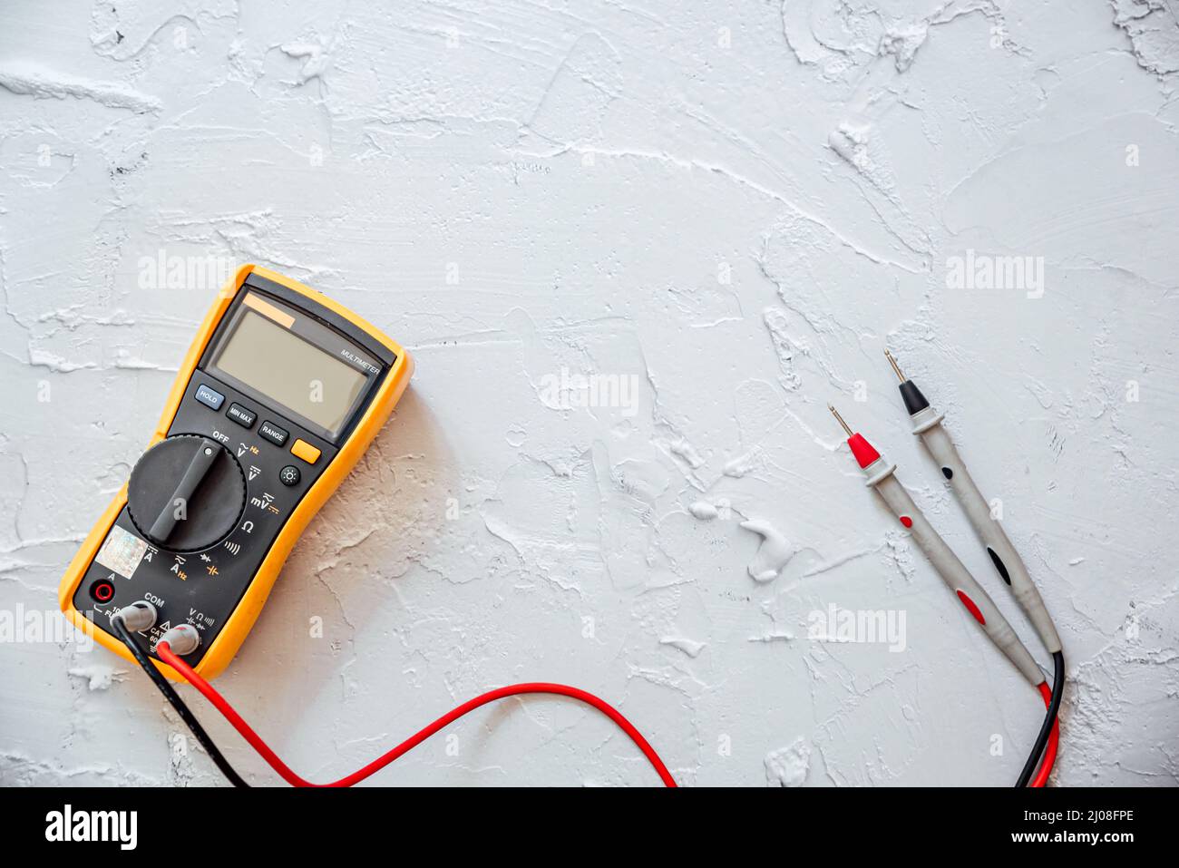 Multimetro digitale giallo con sonde su sfondo bianco con spazio di copia libero. Foto Stock