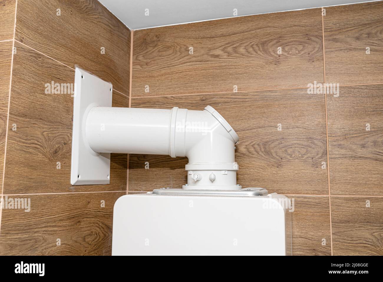 Una moderna caldaia a gas per gas naturale, installata in un locale caldaia rivestito di piastrelle in ceramica, tubo visibile che conduce il gas di scarico al camino. Foto Stock