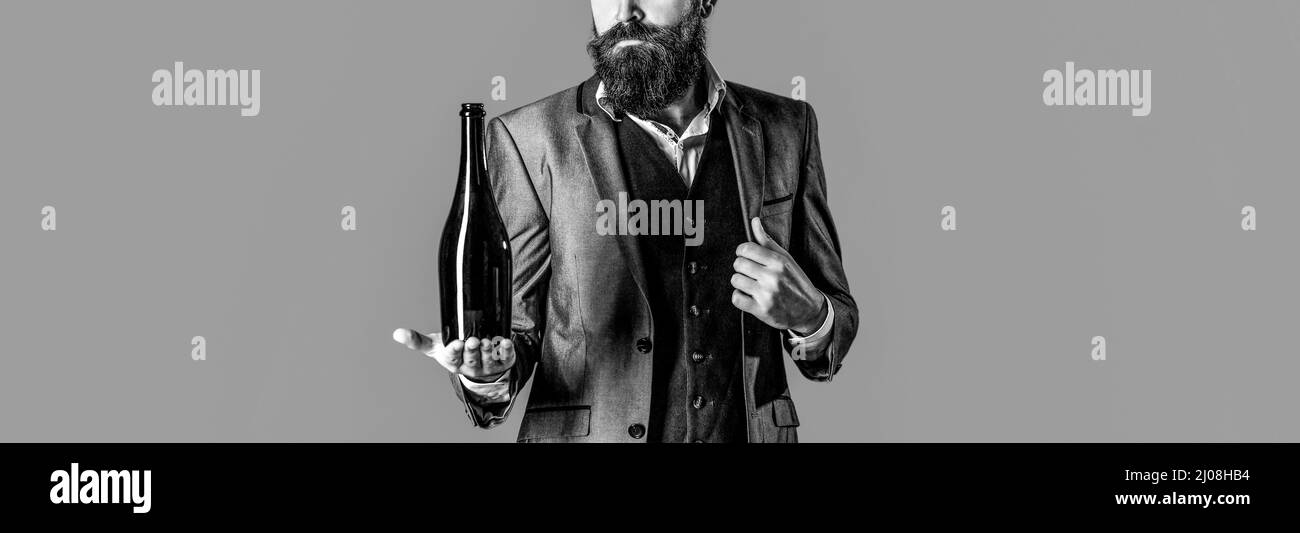 La persona tiene in mano una bottiglia di vino rosso. Uomo che tiene una bottiglia con champagne, vino. Uomo bearded con una bottiglia di champagne e un bicchiere Foto Stock