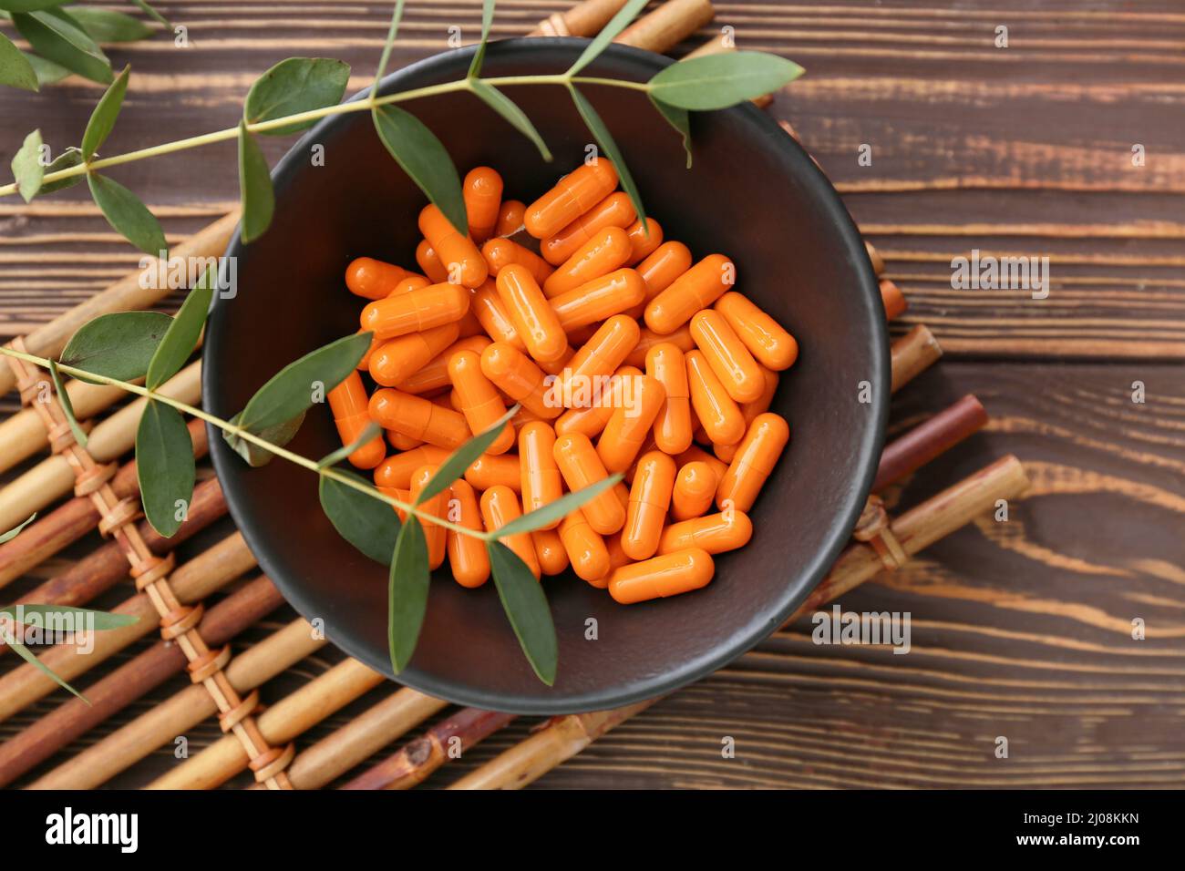 Ciotola con capsule in polvere di curcuma su sfondo di legno Foto Stock