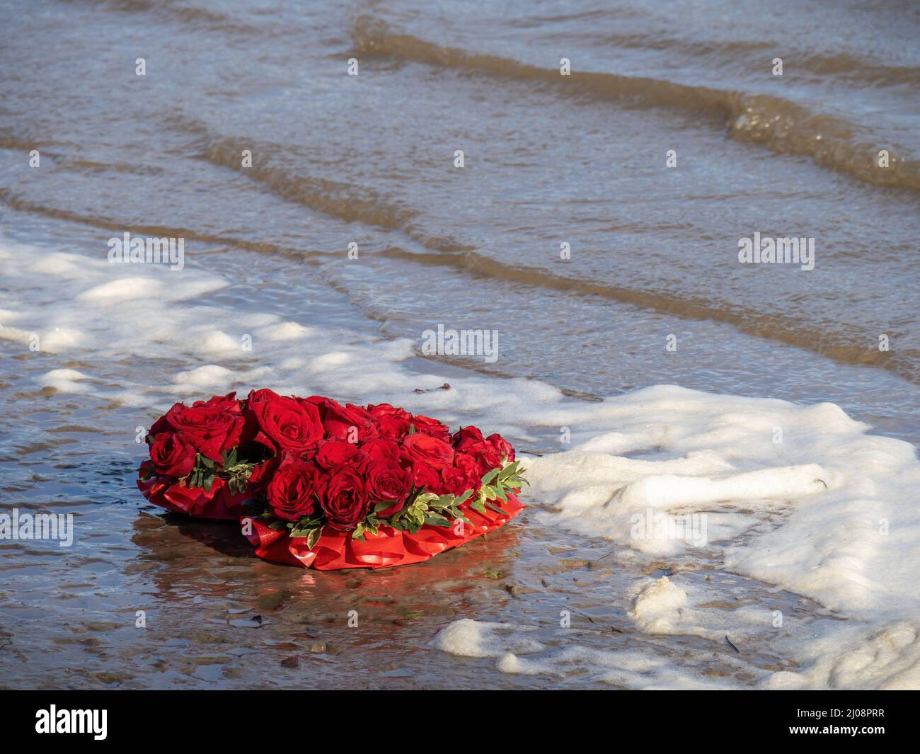 Amore perso forse, corona rossa di rose, annegata dalla marea. Foto Stock