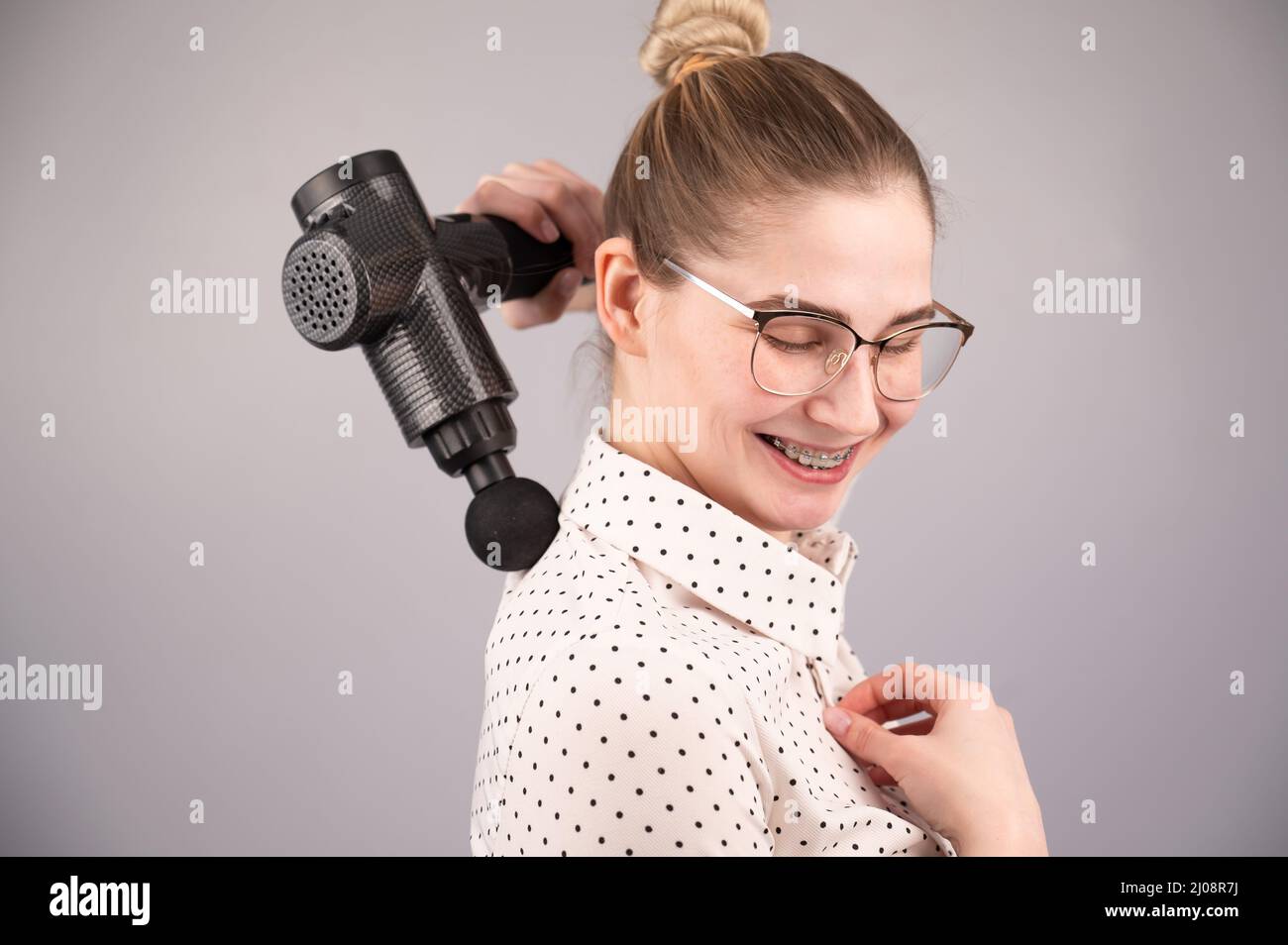 Donna sorridente con bretelle usa una pistola massaggiatore per la schiena. Foto Stock