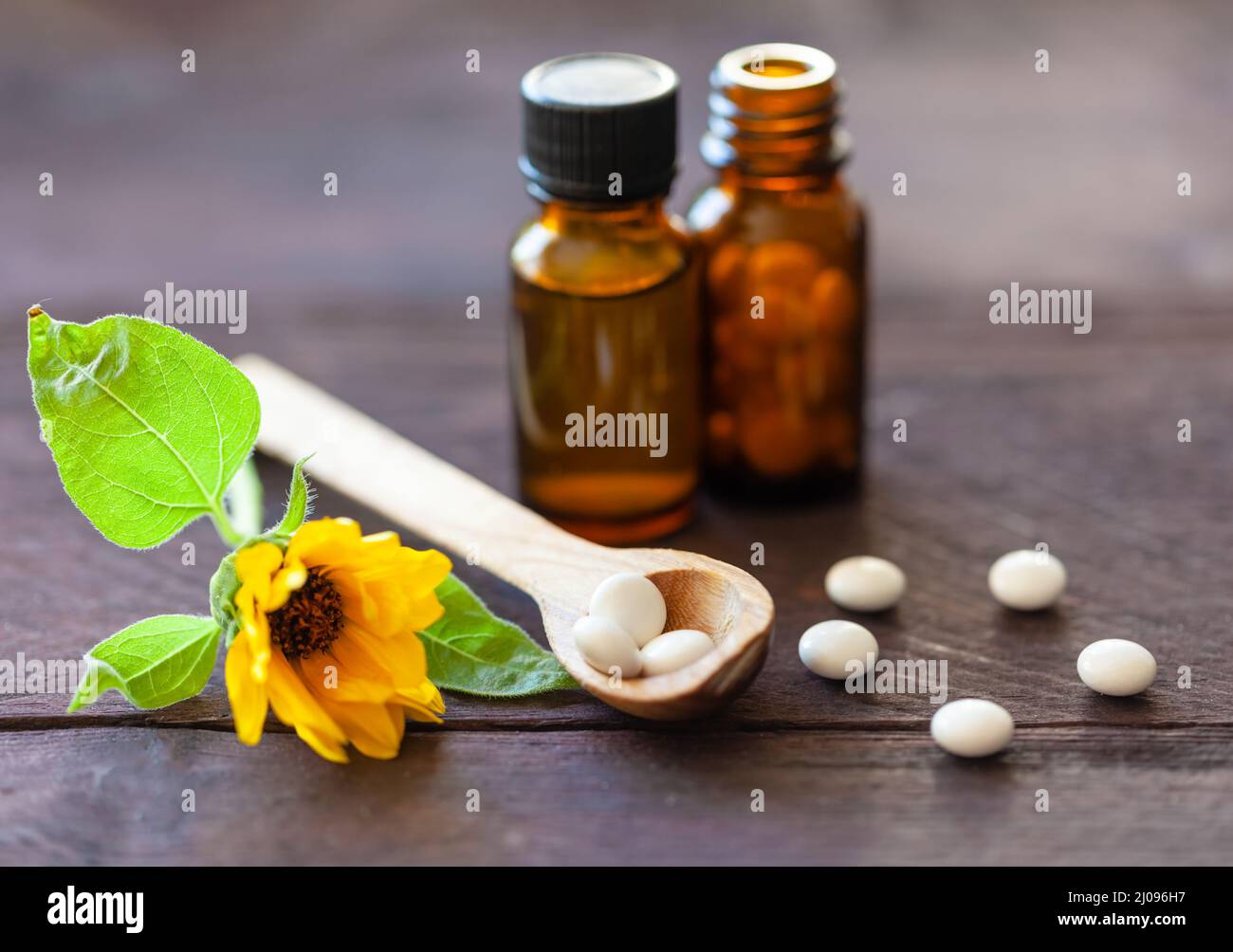 Cucchiaio di legno di pillole omeopatiche, bottiglie e un fiore. Medicina naturale Foto Stock