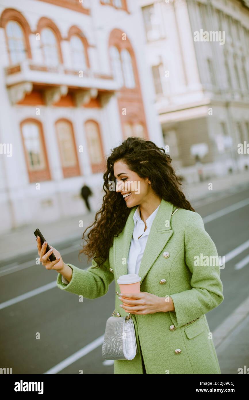 Bella giovane donna che usa lo smartphone per scattare foto selfie in strada e tenere un caffè da asporto Foto Stock