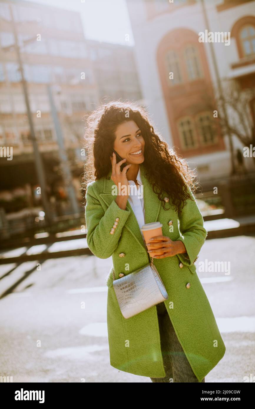 Donna piuttosto giovane che usa lo smartphone per strada e tiene il caffè da asporto Foto Stock