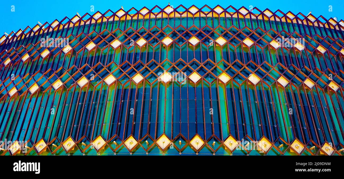 Primo piano ad angolo basso di una recinzione di forma geometrica su un edificio di vetro di tonalità differente Foto Stock