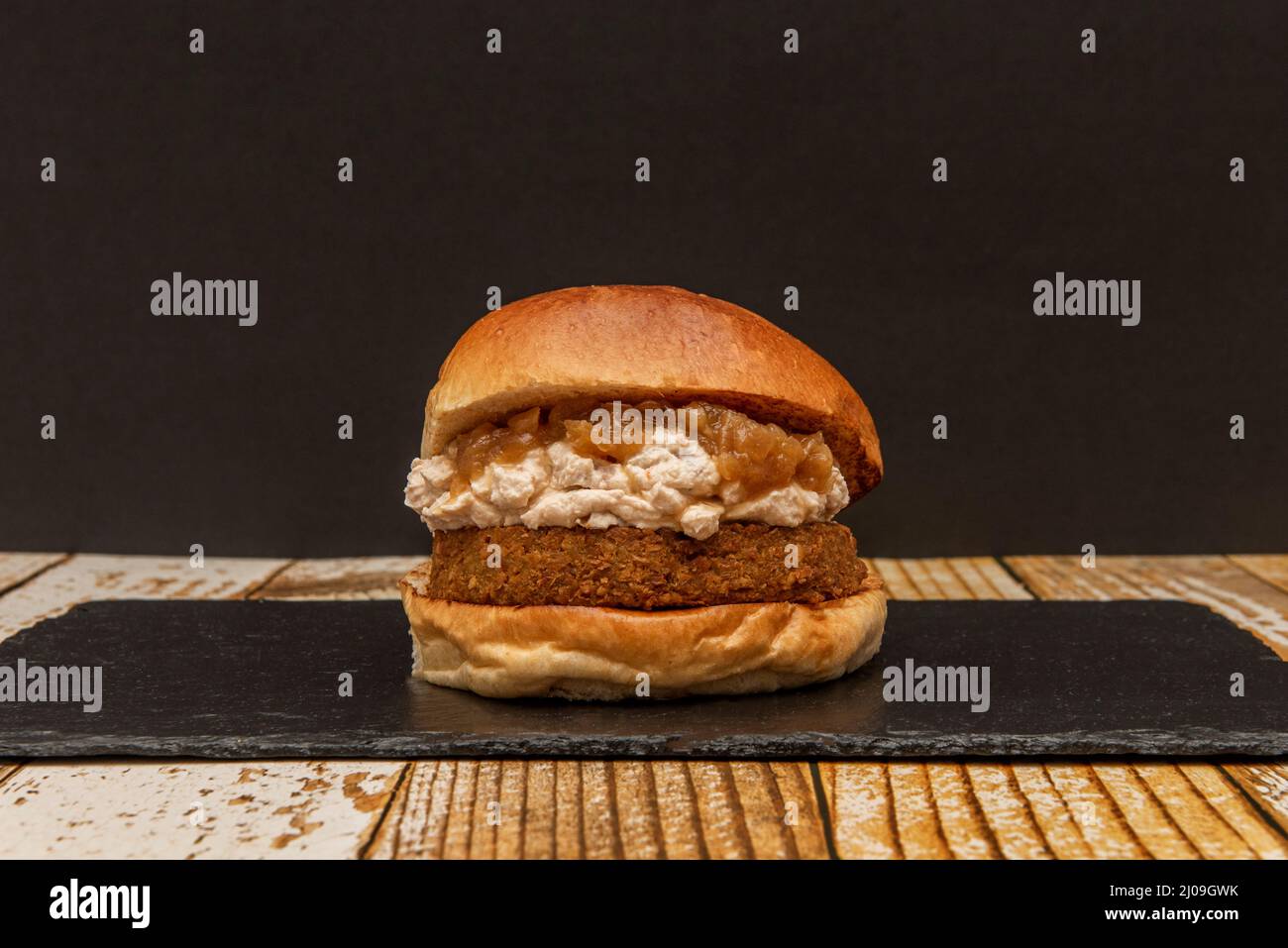 Hamburger di bistecca vegano con panna di piselli e cipolle caramellate su piatto di ardesia nera Foto Stock