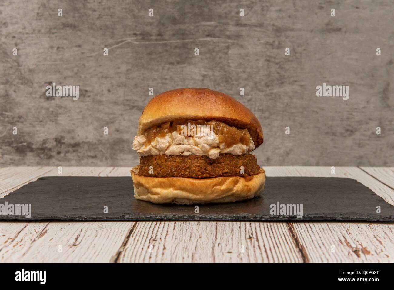 Hamburger di bistecca vegano con cipolle caramellate, panna di ceci con tofu su un piatto di ardesia nera Foto Stock