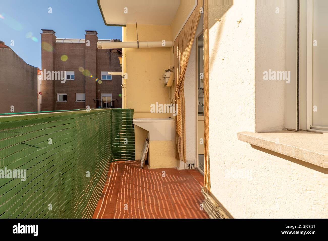 terrazza con lavello in porcellana per il lavaggio a mano in una casa residenziale urbana con griglia di plastica verde sulla ringhiera Foto Stock