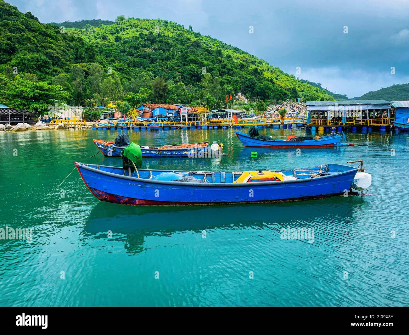 Piccole barche da pesca blu ormeggiate intorno ai moli presso i ristoranti di pesce. Foto Stock