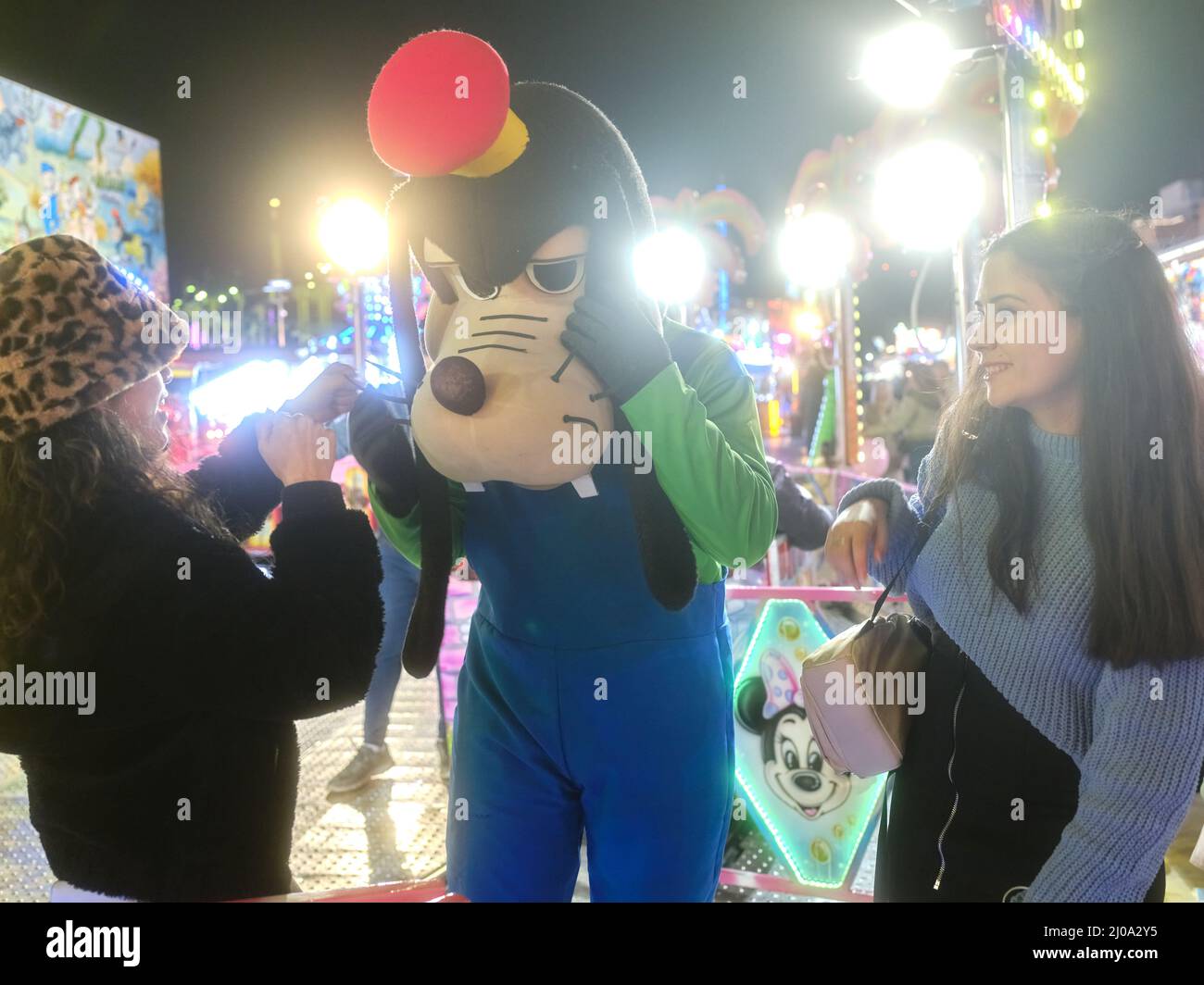 Donne che scherzano con un attore vestito come cane in un parco a tema Foto Stock