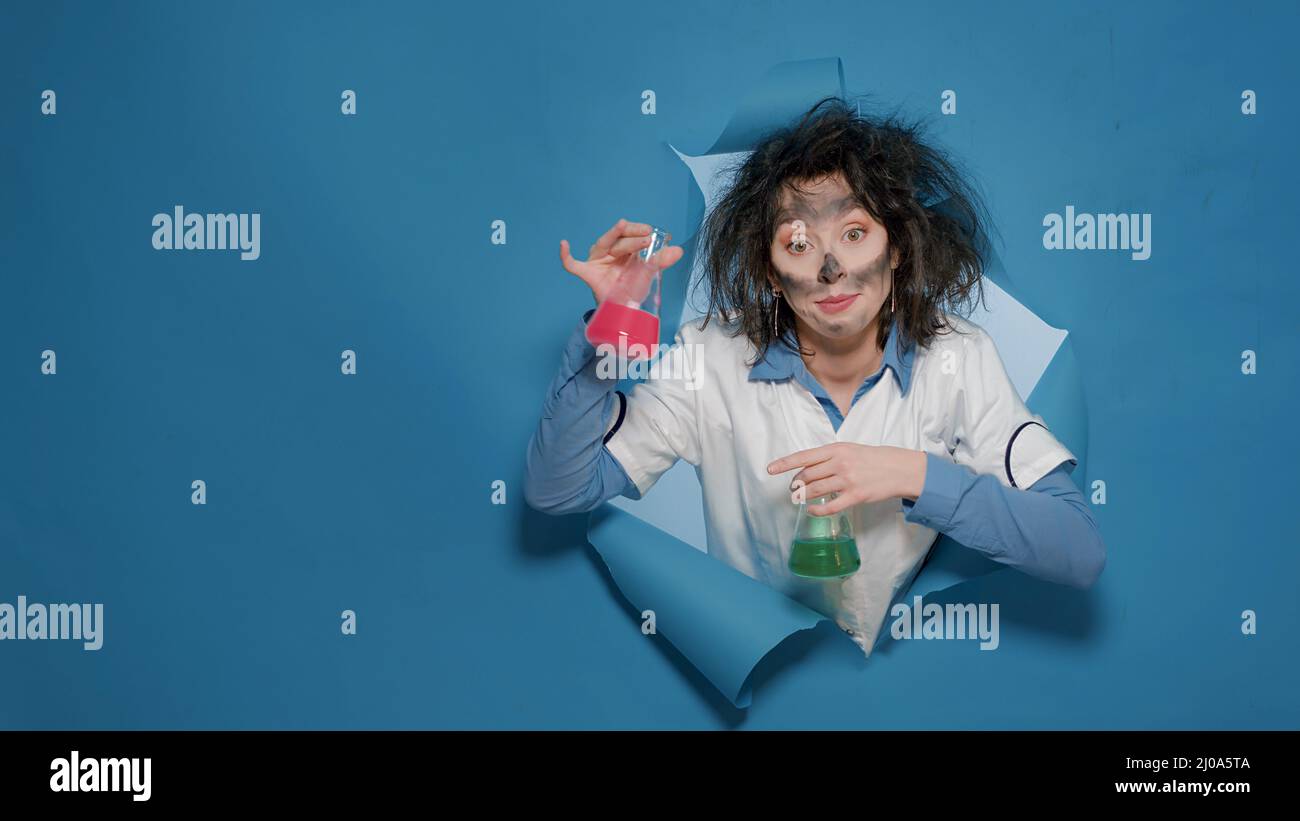 Sciocco chimico pazzo che fa la grimace sciocca e becher di tenuta dopo l'esplosione chimica insana. MAD goofy chemist avere capelli disordinati e divertente divertente divertente espressioni facciali in studio. Foto Stock