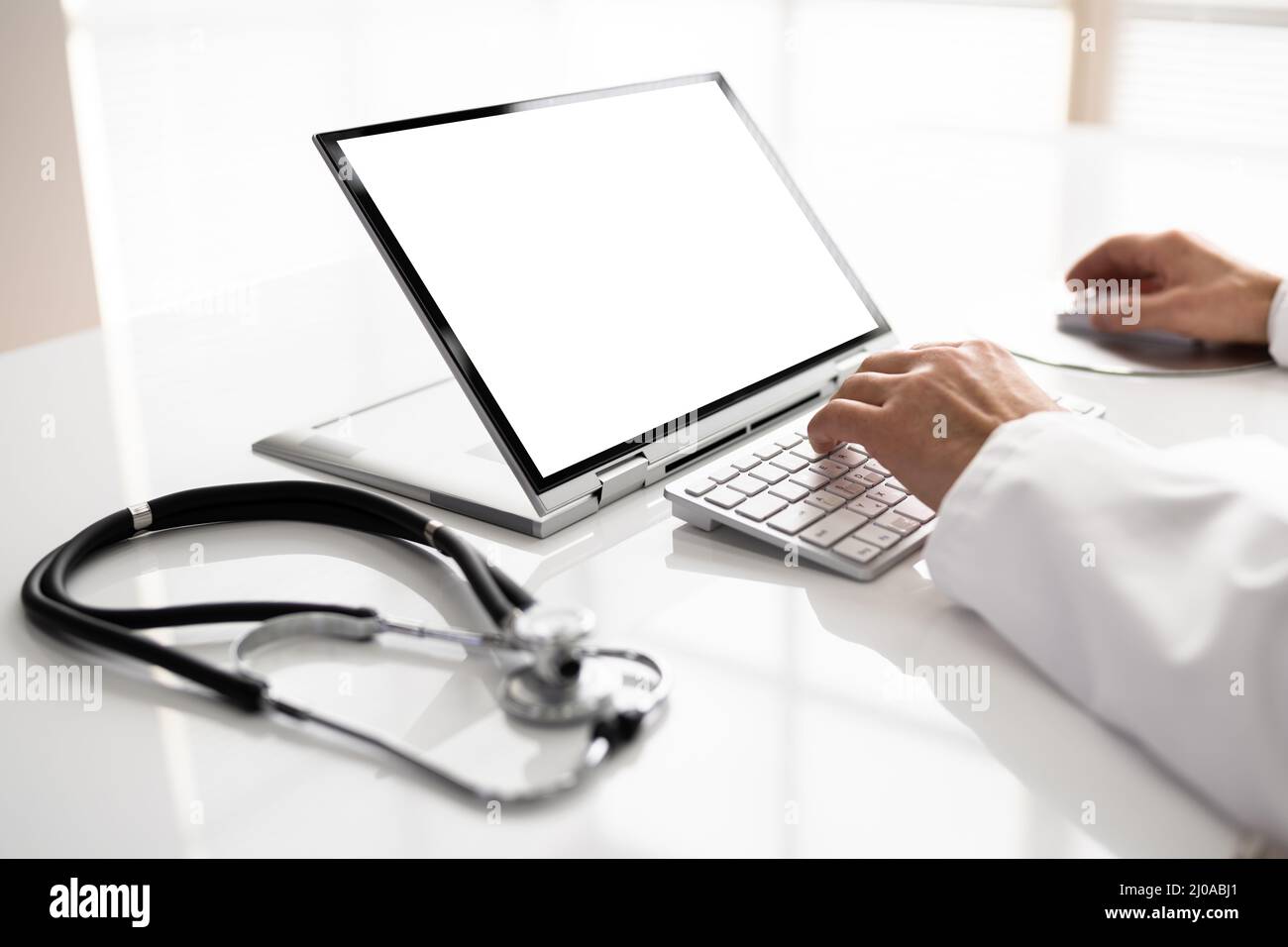 Sezione Centrale Di Male Doctor Using Laptop At Desk In Clinic Foto Stock
