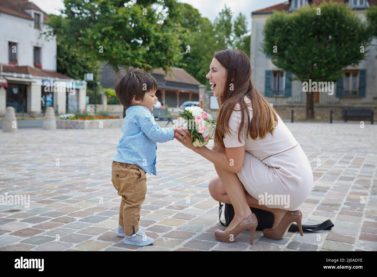 Ragazzo di razza mista figlio piccolo congratularsi con sua mamma e dare il suo bouquet di fiori, abbracciando e ridendo insieme. Concetto di vacanza in famiglia Foto Stock