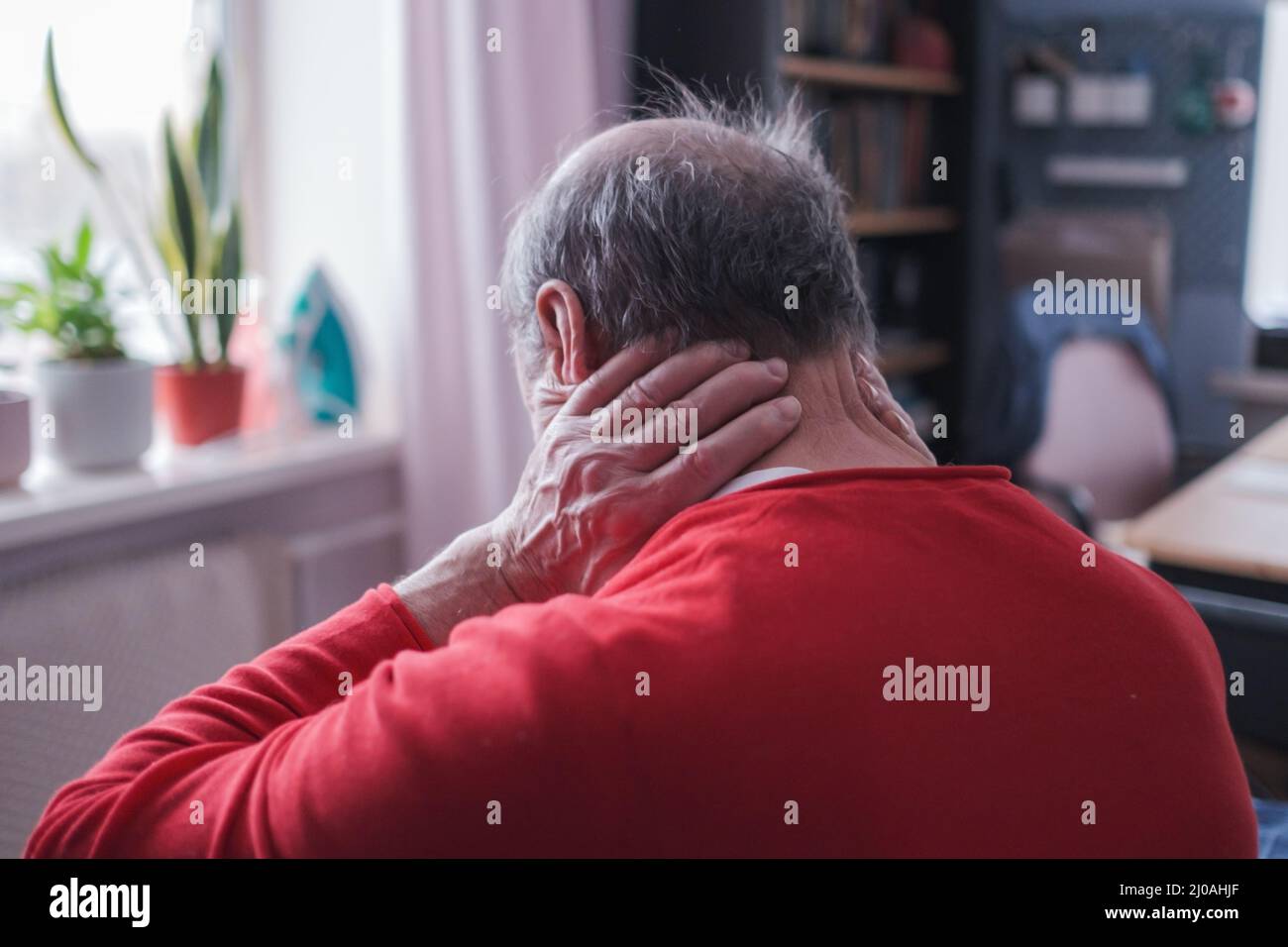 Ho bisogno di un massaggio. Uomo anziano frustrato in maglione rosso che tiene la mano sul collo seduto sul divano Foto Stock Ho bisogno di un massaggio. Uomo anziano frustrato in maglione rosso che tiene la mano sul collo seduto sul divano Foto Stock