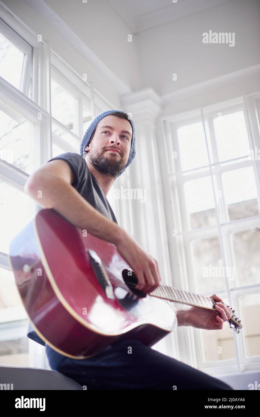 Padroneggiare le sue abilità musicali. Scatto corto di un bel giovane che suona una chitarra a casa. Foto Stock