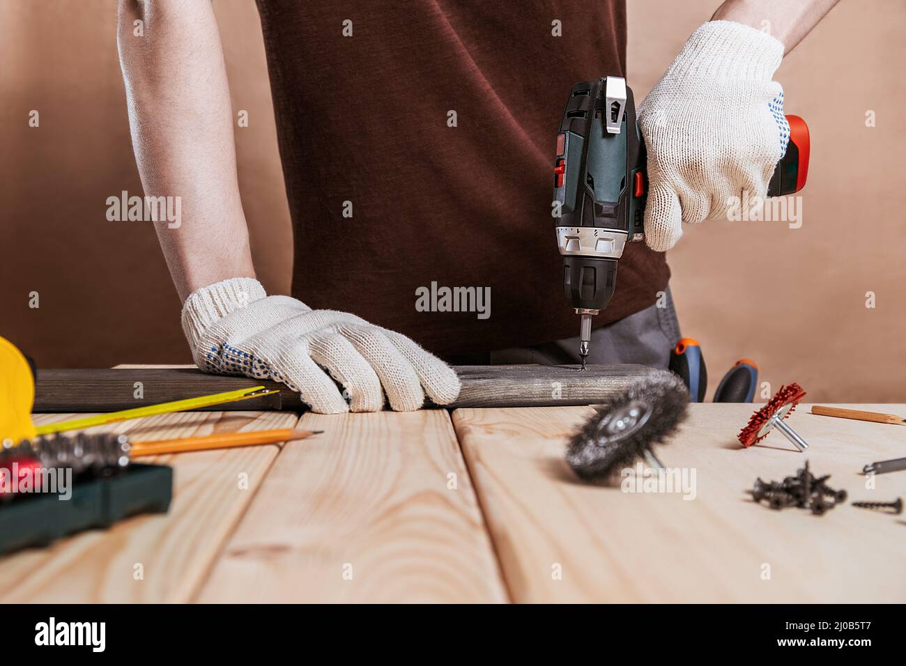 Primo piano ritratto e dettagli di lavoratore caucasico maschio utilizzando strumento cacciavite elettrico in mano e riparazione di nuovo scrivania in legno, miglioramento casa c Foto Stock