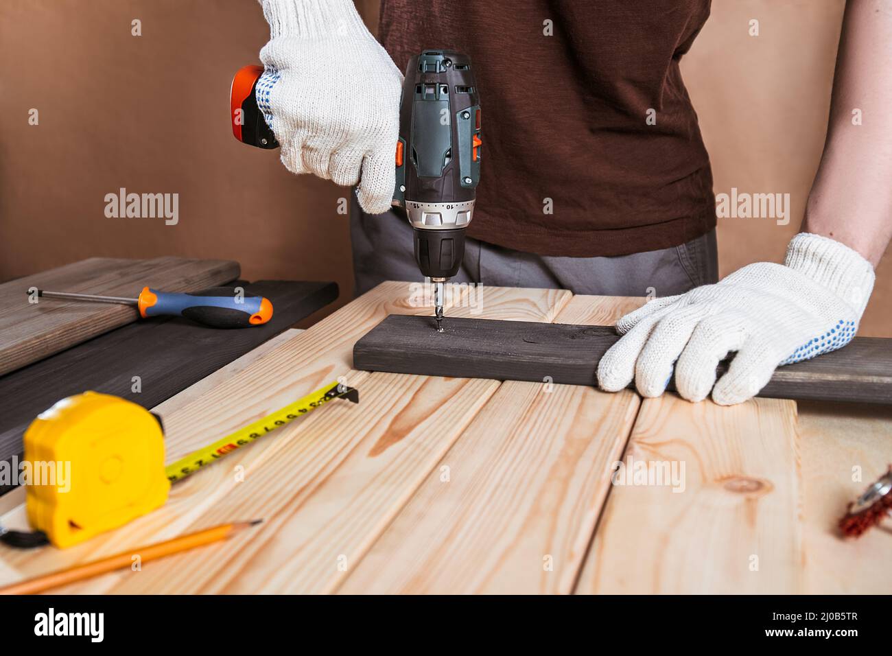Primo piano ritratto e dettagli di lavoratore caucasico maschio utilizzando strumento cacciavite elettrico in mano e riparazione di nuovo scrivania in legno, miglioramento casa c Foto Stock