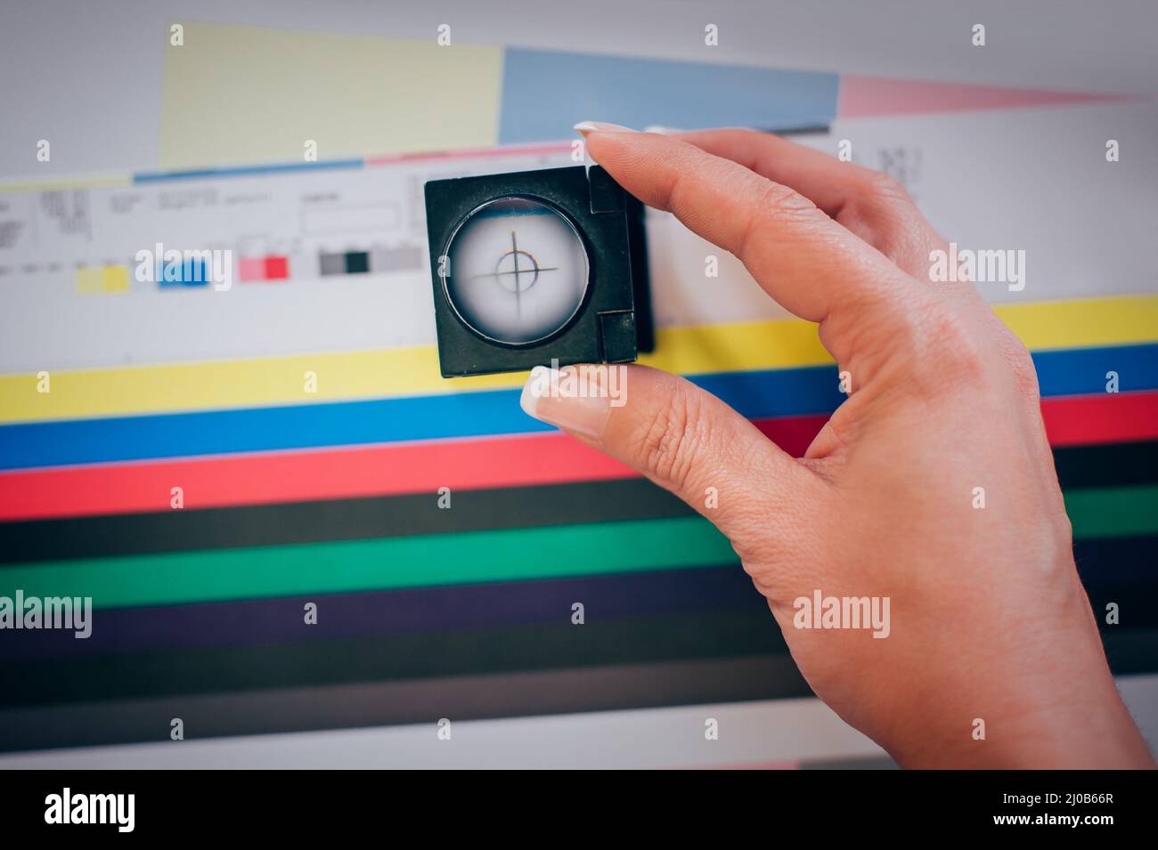 Chi lavora in una stampa e preme centar utilizza una lente di ingrandimento per verificare la qualità di stampa Foto Stock
