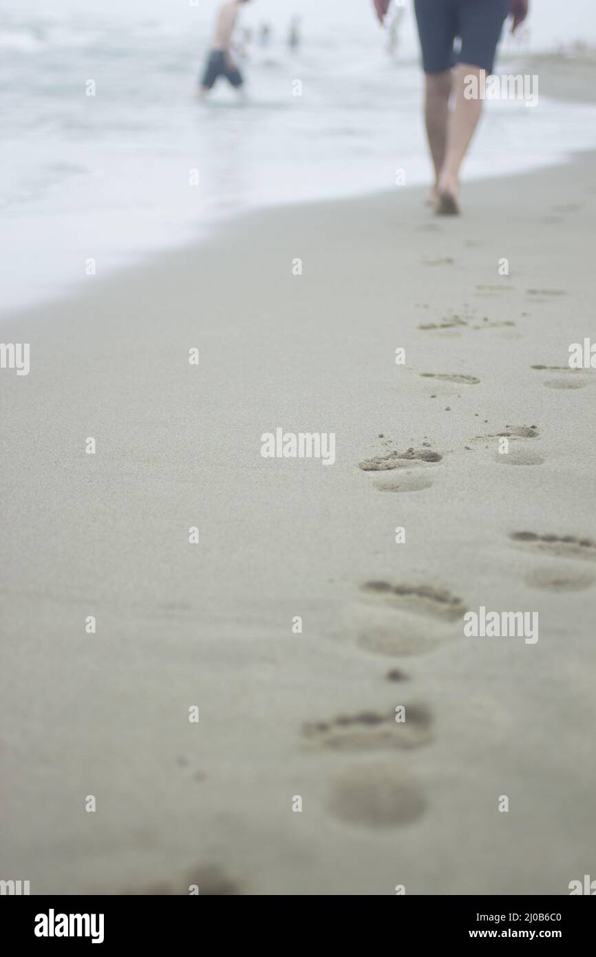 Gambe di uomo e impronte sulla sabbia della spiaggia Foto Stock