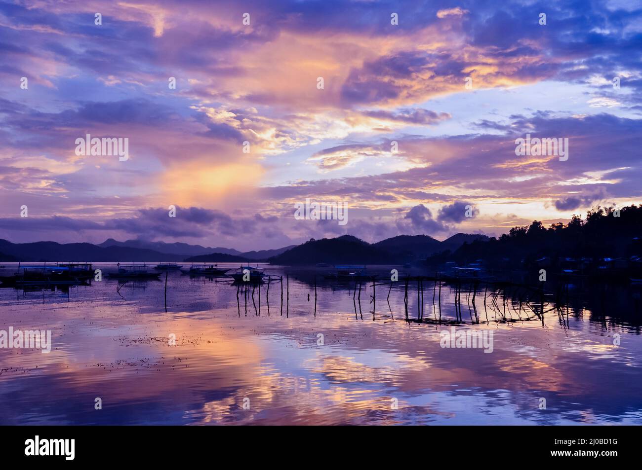 Grazioso paesaggio di cielo arancione rosa su un'isola con riflessi e tradizionali barche filippine in legno al tramonto sull'isola o Foto Stock