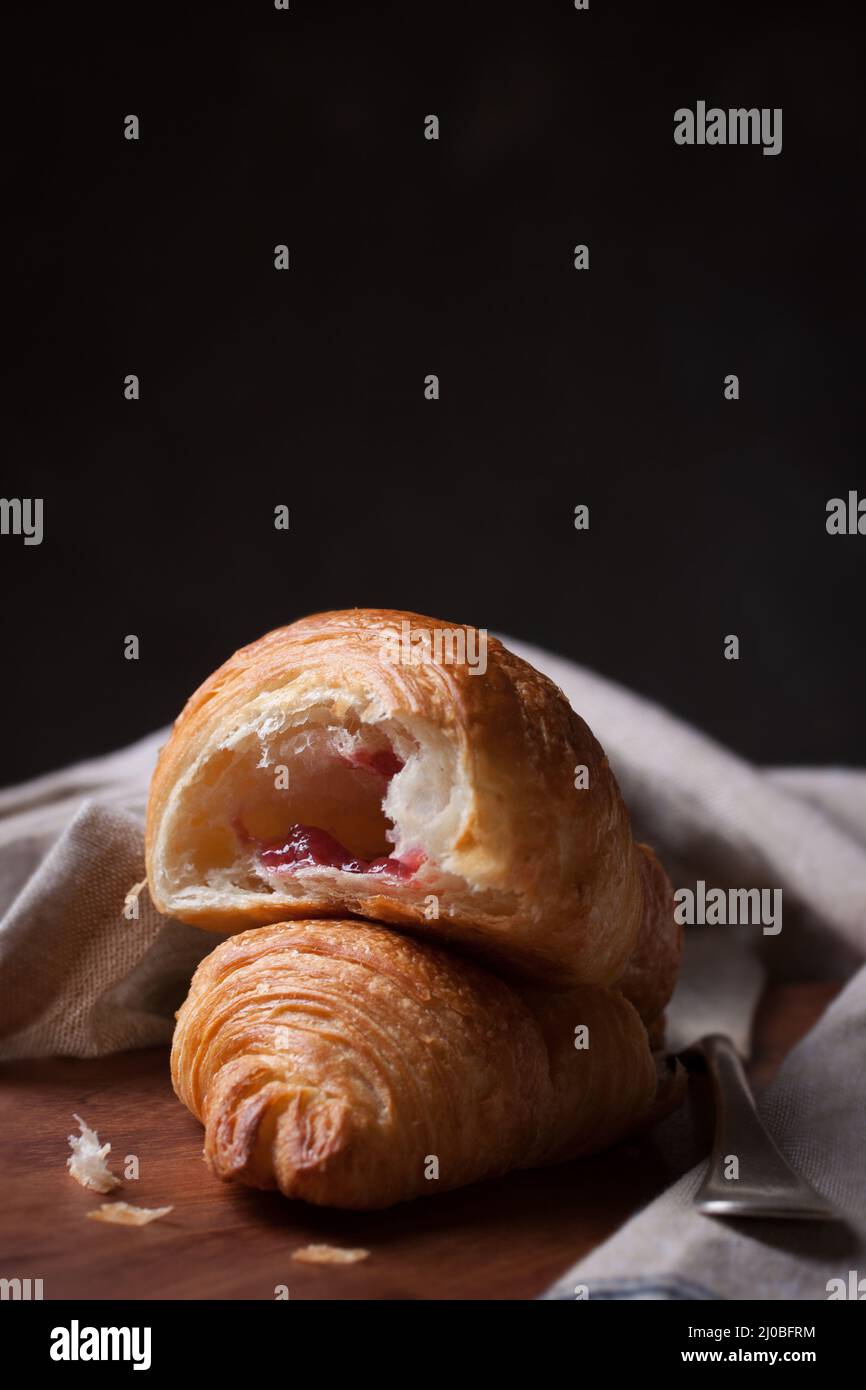 Primo piano di croissant con marmellata e coltello su sfondo di legno Foto Stock