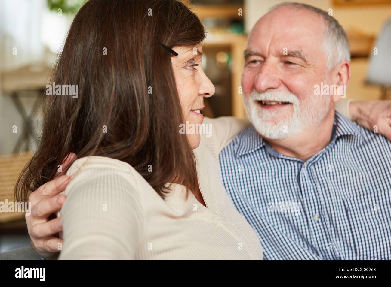 Coppia anziana che si guarda negli occhi felicemente e amorevolmente sul divano a casa Foto Stock