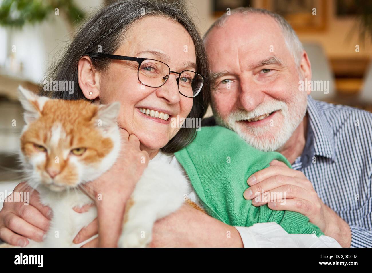 Coppia anziana felice con il loro gatto sulle braccia a casa per la compagnia e l'amore per gli animali Foto Stock