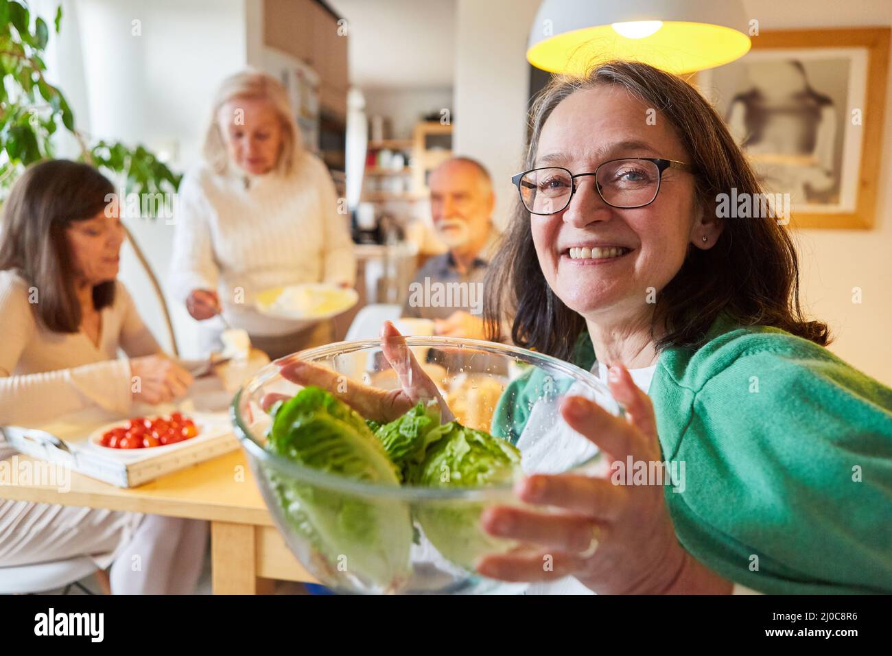 Donna anziana che tiene una ciotola di insalata fresca per un brunch sano con gli amici in cucina Foto Stock