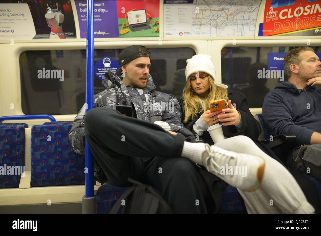 Londra, Inghilterra, Regno Unito. Le persone su un treno della metropolitana che guardano i loro telefoni cellulari Foto Stock