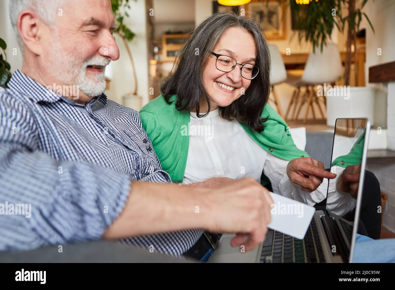 Coppia anziana che si diverte a fare shopping online con carta di credito sul computer portatile a casa Foto Stock