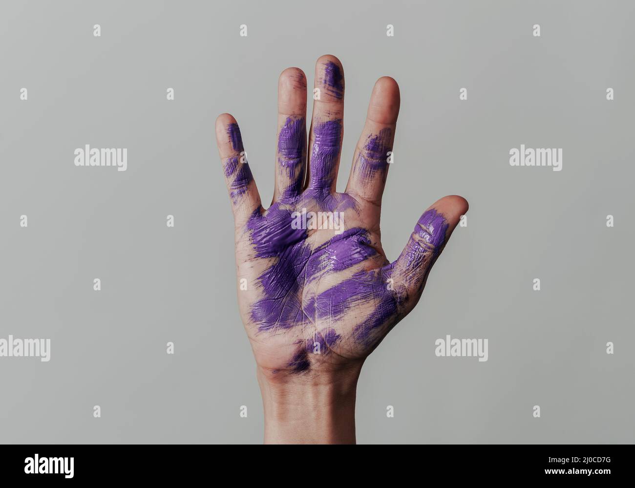 primo piano della mano sollevata di un uomo con alcune macchie di vernice viola nel palmo, su sfondo grigio chiaro Foto Stock