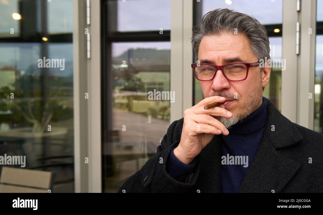 Sigaro uomo di mezza età fumatori all'aperto di fronte all'edificio degli uffici. Foto Stock