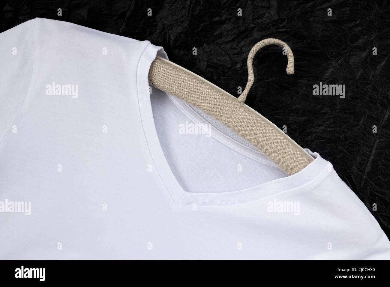 Una t-shirt in cotone bianco, appendiabiti in lino. Primo piano, sfondo nero Foto Stock