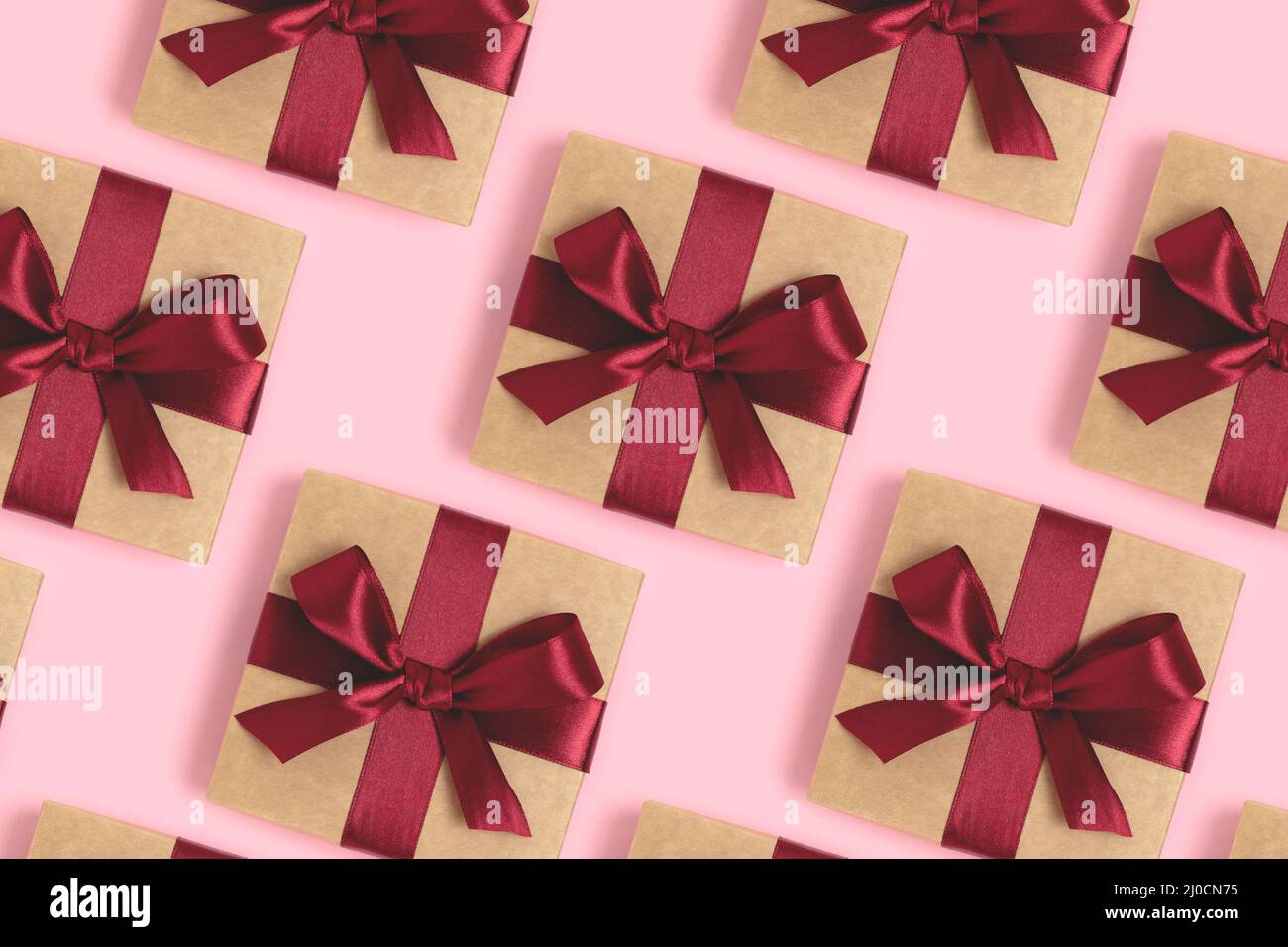 Modello ripetitivo fatto di scatole regalo legato con nastri rossi su uno sfondo rosa. Concetto di vacanza. Foto Stock