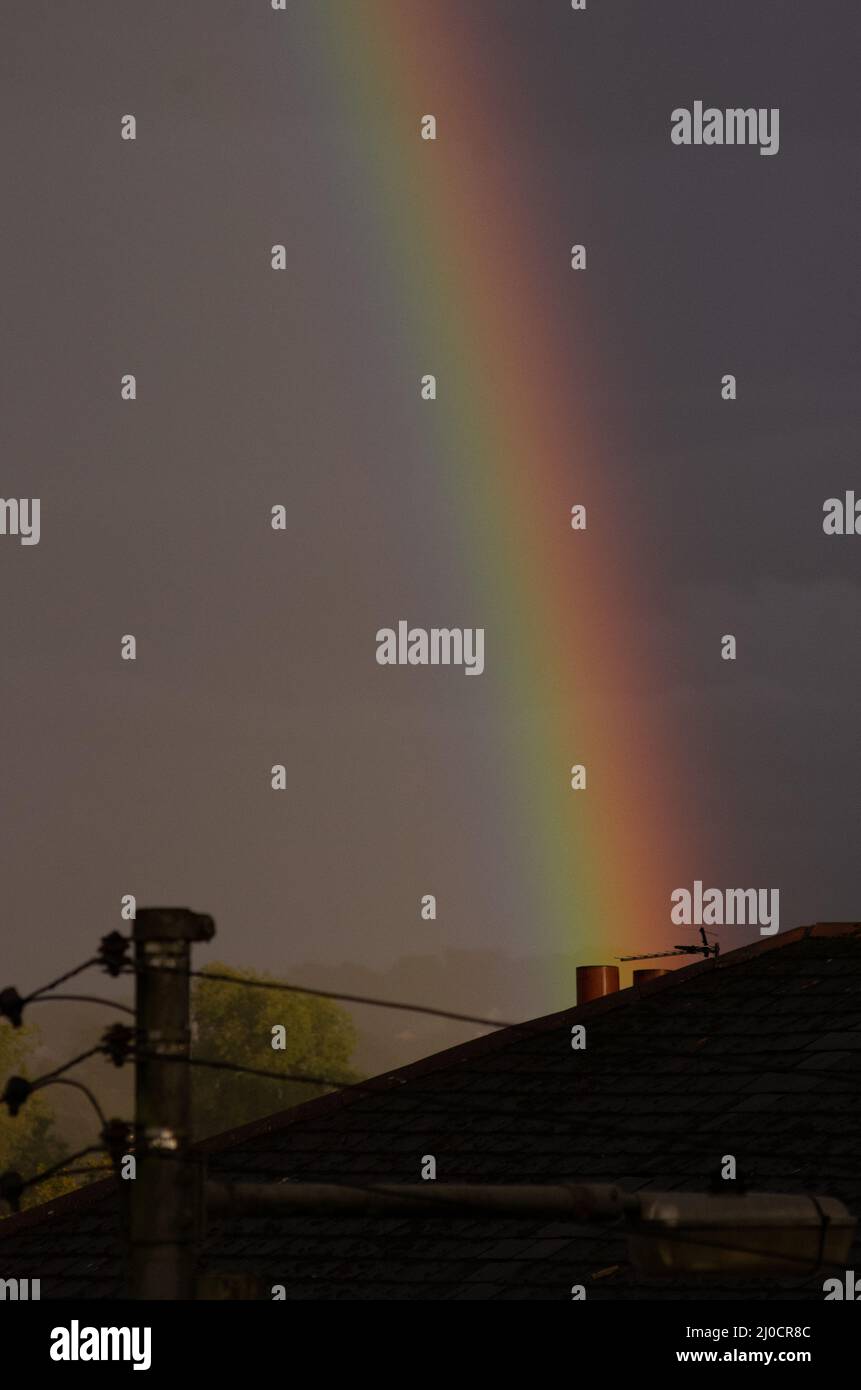 Arcobaleno che sorge dietro i pentole di camino su un tetto Foto Stock