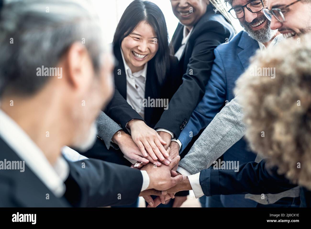 Uomini d'affari multirazziali che si accatastano le mani insieme in un ufficio moderno - concetto di lavoro di squadra Foto Stock