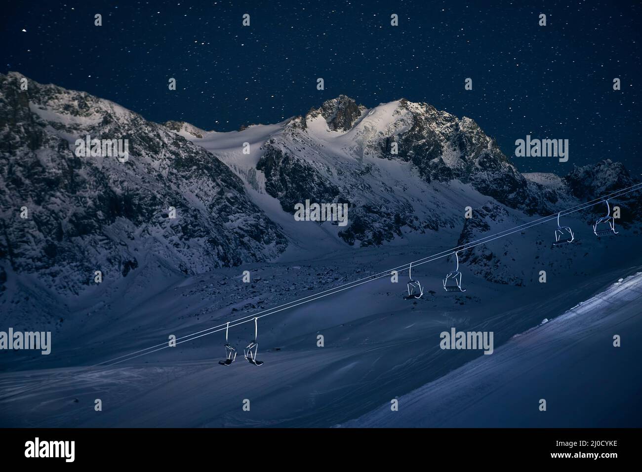 Funivia vuota e pista da sci al parco notturno con alta montagna contro il cielo stellato presso la stazione sciistica di Shymbulak Almaty, Kazakhstan Foto Stock