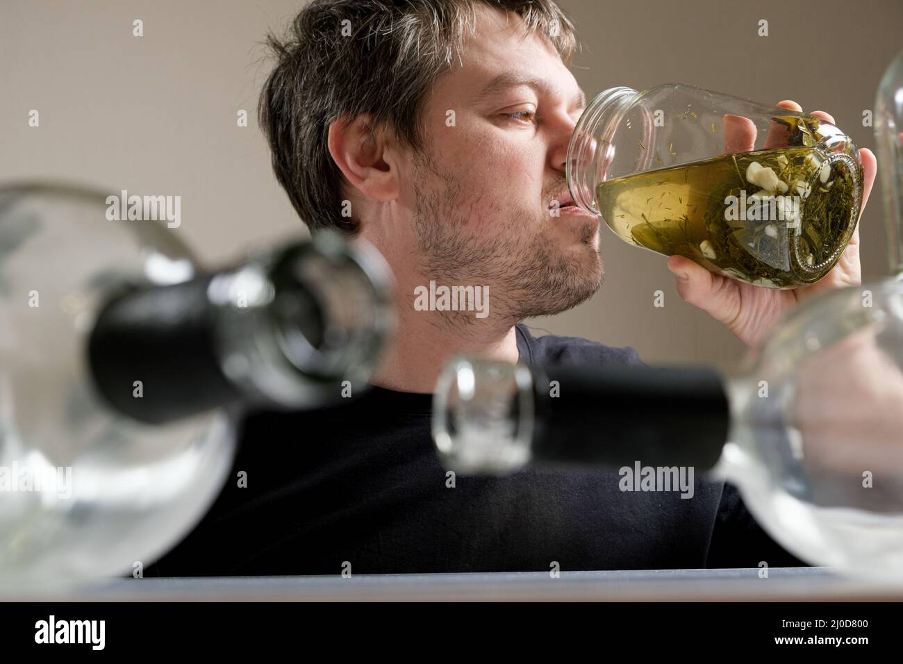 Un uomo con dipendenza da alcol beve salamoia da un vaso di cetrioli di Aole, un uomo in un hangover. Foto Stock