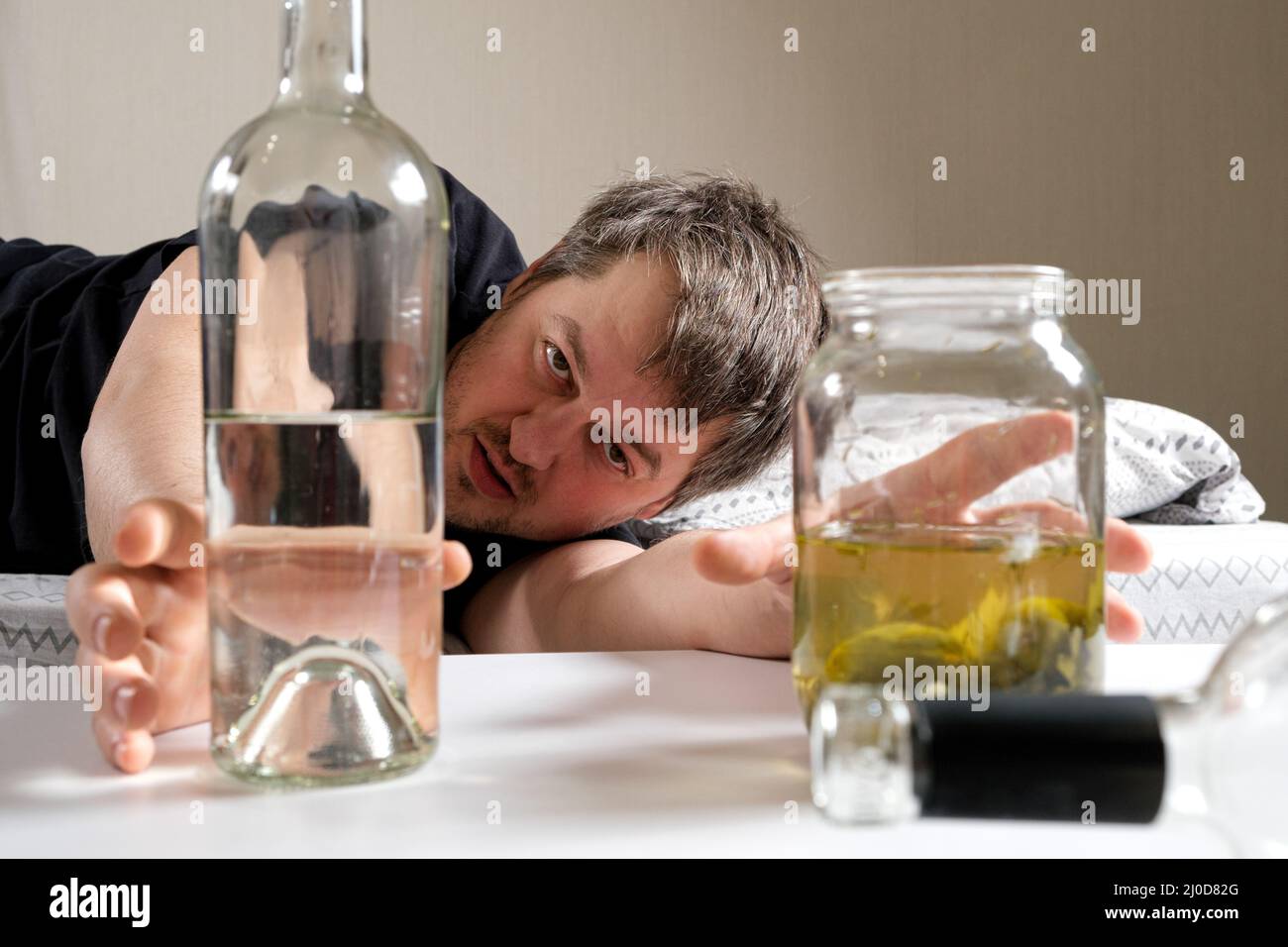 Un uomo ubriaco con dipendenza da alcol prende una bottiglia di vodka e salamoia con sottaceti sottaceto. Foto Stock