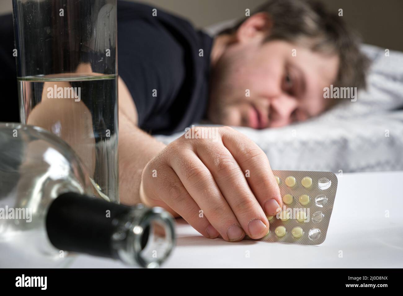 Un uomo si trova su un letto dopo una festa di alcol, tenendo in mano le pillole di hangover Foto Stock