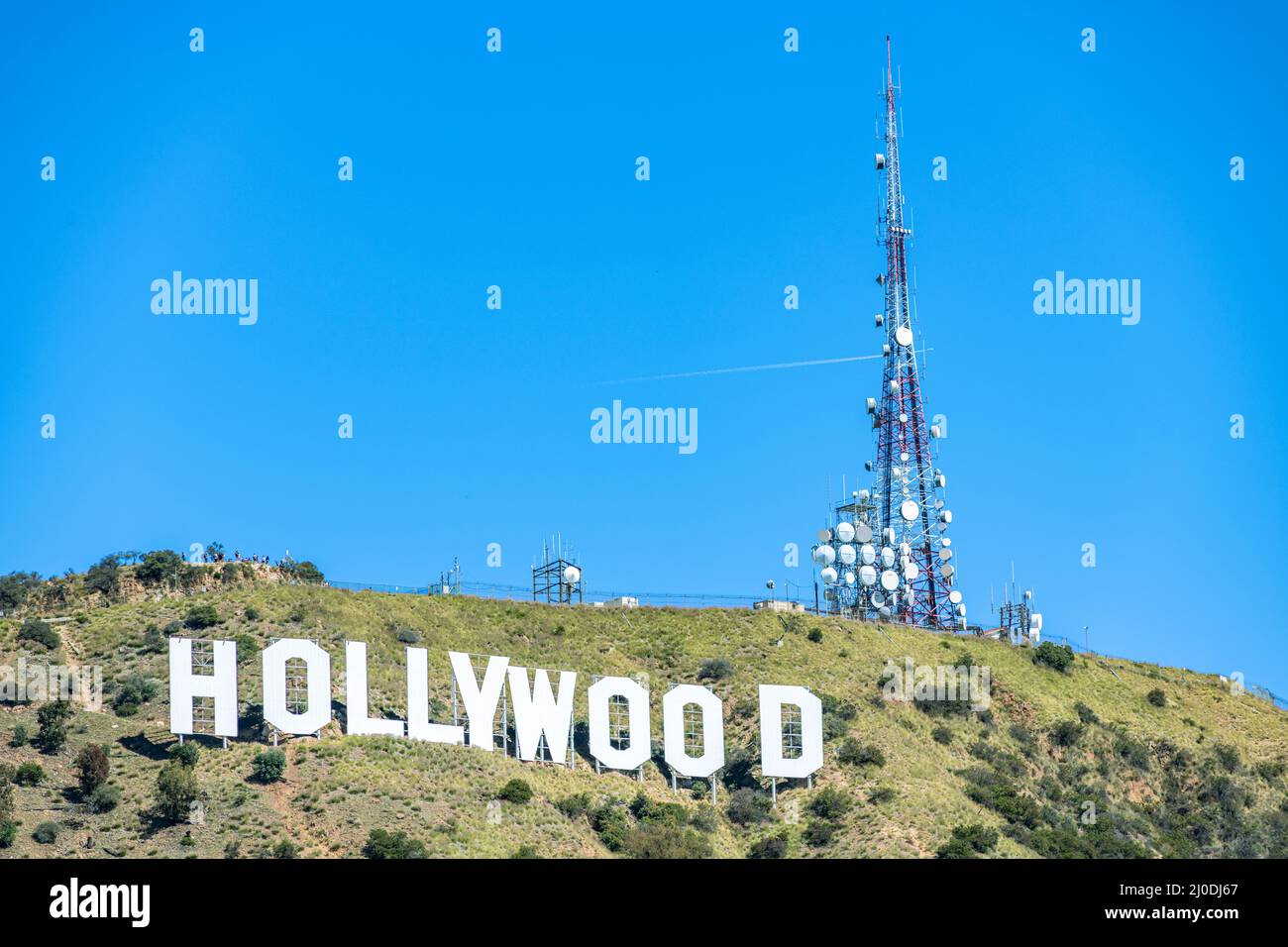 Il famoso segno bianco di Hollywood nelle colline di Los Angeles, California incorniciata da una torre cellulare massiccia e cielo blu brillante. Foto Stock