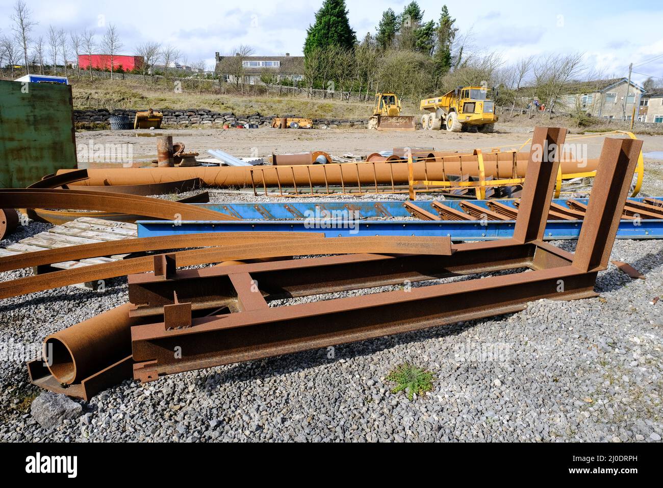 Scartato, arrugginito con un mix di arancione e blu che giace in un cantiere. Un camion giallo e alloggi privati sono sullo sfondo. Foto Stock