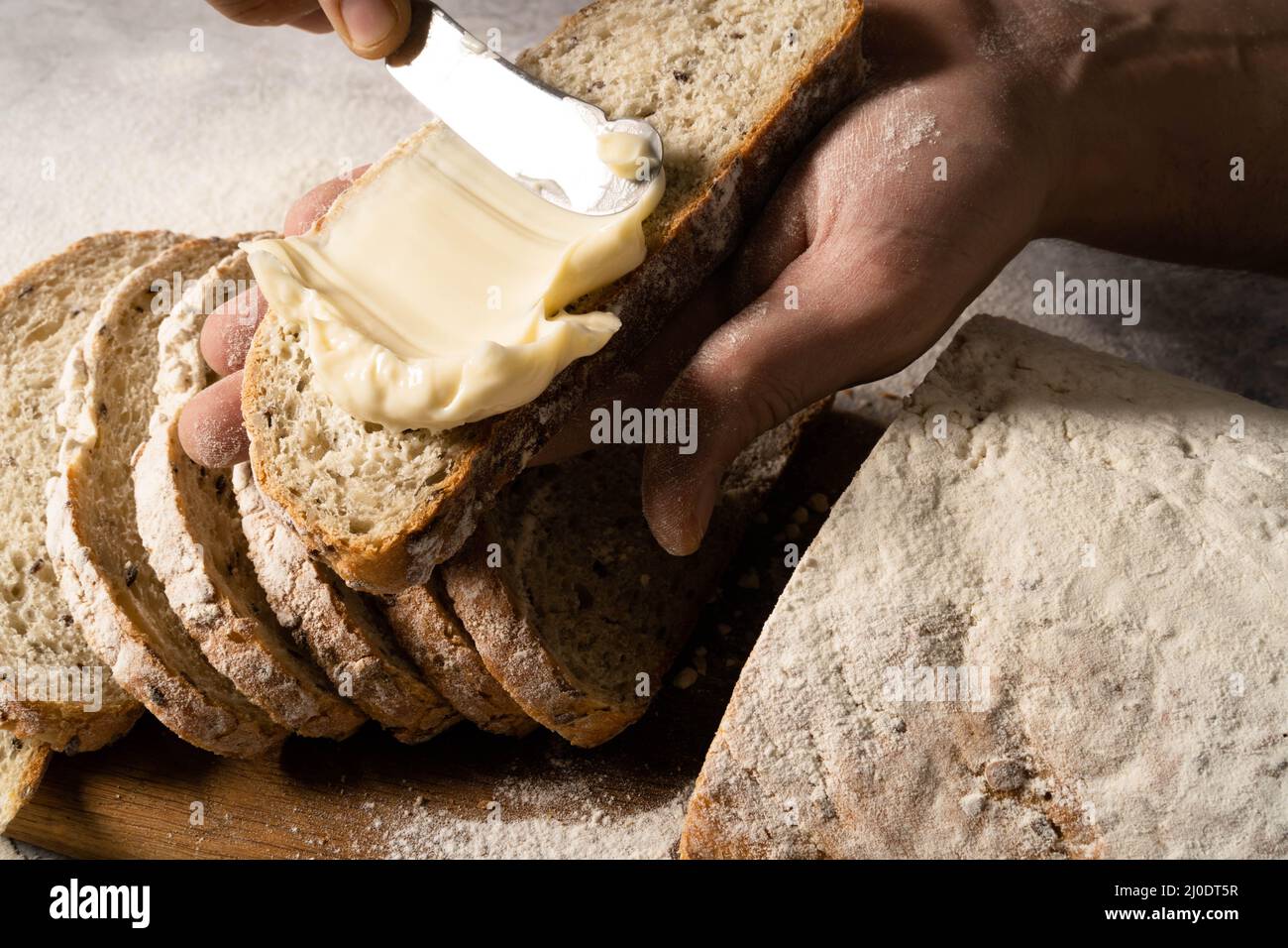Uomo spalmando burro di formaggio cremoso o una fetta di pane su tavola di legno. Pane da dieta. Primo piano. Concetto di nutrizione sana. Foto Stock